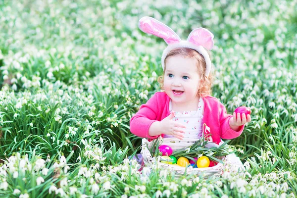 Flicka som leker med påskägg i en vit korg som sitter i en solig trädgård — Stockfoto