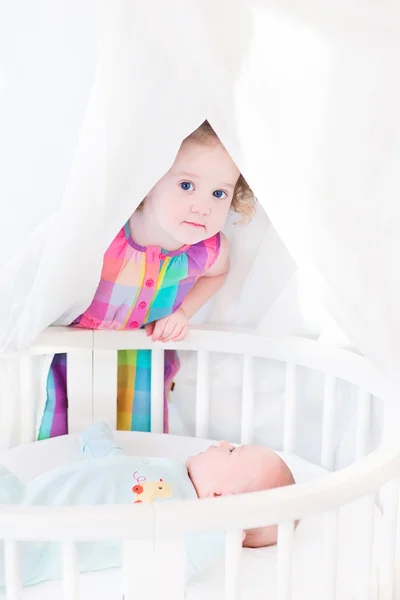 Toddler girl hiding from her newborn baby brother — Stock Photo, Image