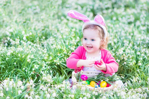 Девушка играет с пасхальными яйцами в белой корзине, сидя в солнечном саду — стоковое фото