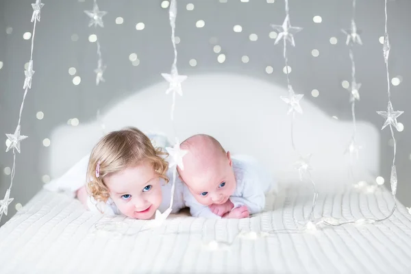 Nyfødt baby og lille søster leger på en hvid seng - Stock-foto