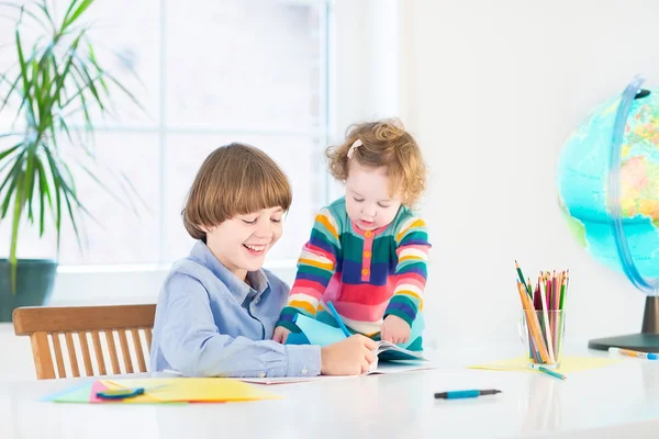 Szkole chłopiec robi swoją pracę domową i jego siostra maluch patrzy na niego — Zdjęcie stockowe