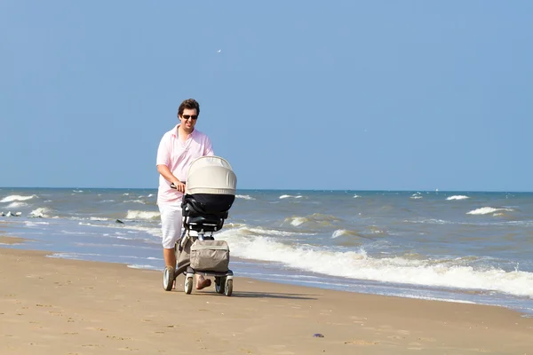 Vader wandelen met een kinderwagen op een strand — Stockfoto