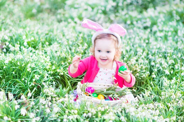Dziewczyna bawi sie z jaja wielkanocne w biały kosz siedzący słoneczny ogród — Zdjęcie stockowe