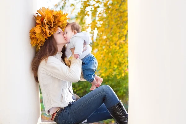 Mother with maple leaves wreath kissing her baby — Stock Photo, Image