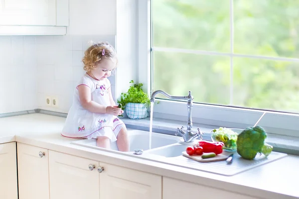 Toddler girl washing vegetables in a kitchen sink — Stock Photo, Image