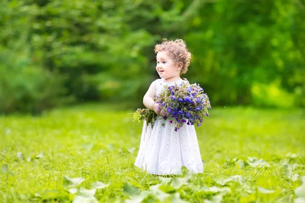 Baby girl with curly hair carrying flowers — Stock Photo, Image