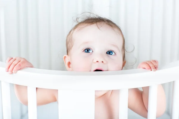 Little baby standing in a round white crib — Stock Photo, Image