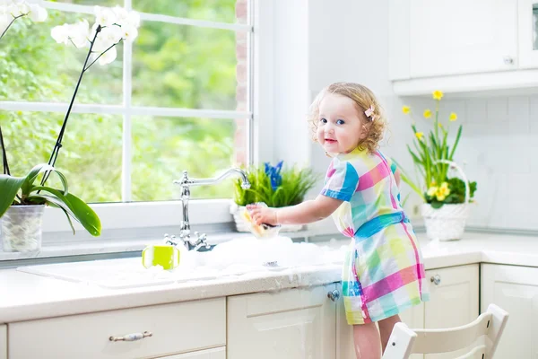 Chica lavando platos, limpiando con una esponja y jugando con espuma —  Fotos de Stock
