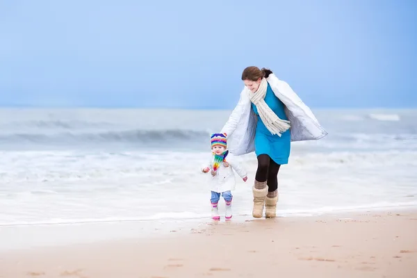 Madre e sua figlia bambina corrono insieme su una spiaggia invernale — Foto Stock