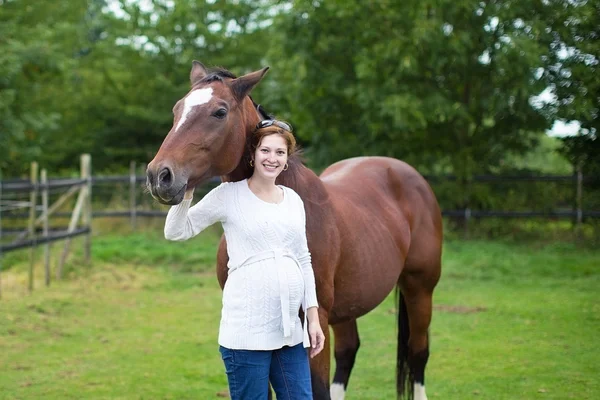 Gravid kvinna och en häst som står i ett fält — Stockfoto