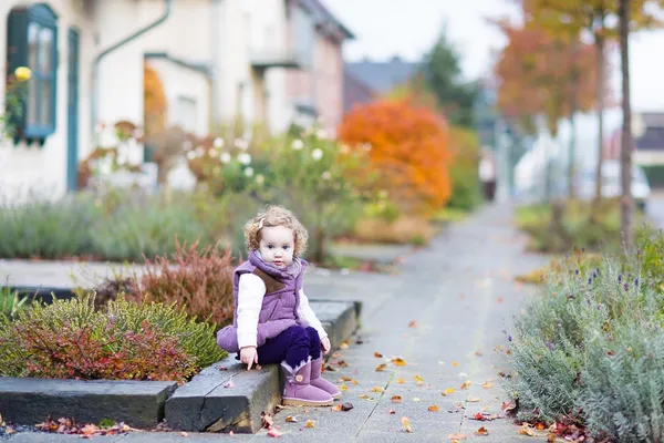 Toddler girl sitting on the front yard of  house