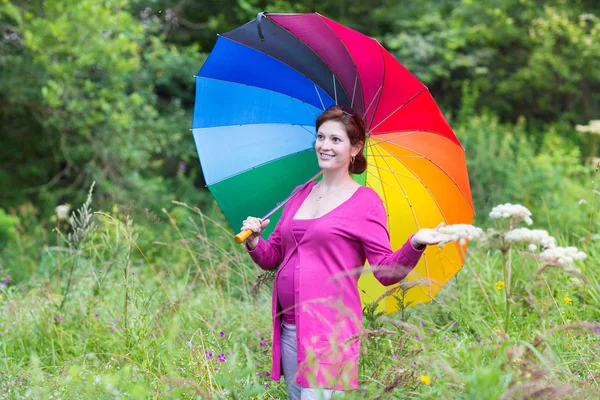 Mulher grávida andando sob um guarda-chuva colorido — Fotografia de Stock