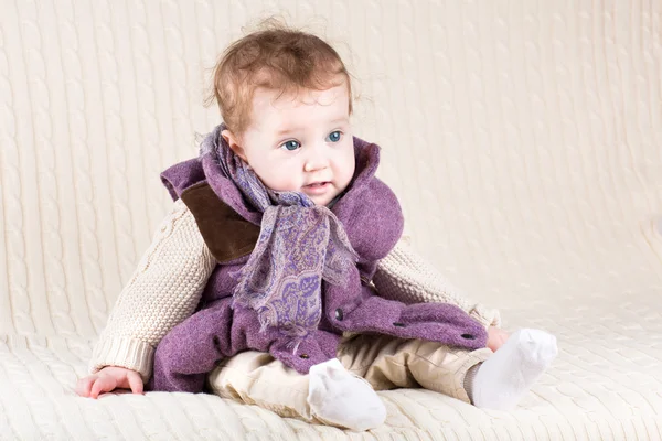 Baby girl in a purple jacket sitting on a knitted — Stockfoto