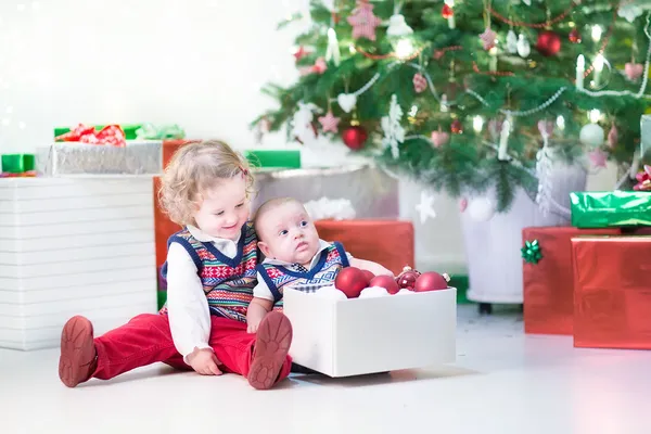 Toddler girl and her newborn brother helping to decorate a Christmas tree Royalty Free Stock Images