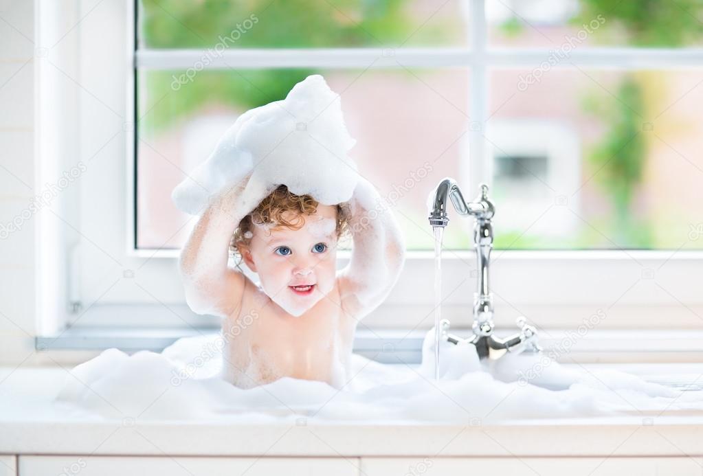 Baby girl with big blue eyes playing in a bath