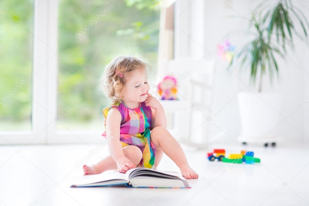 Toddler girl reading a book in a sunny bedroom