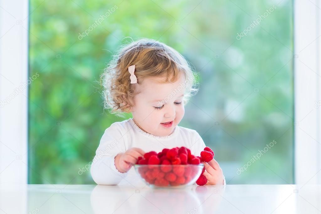Cute toddler girl eating raspberries