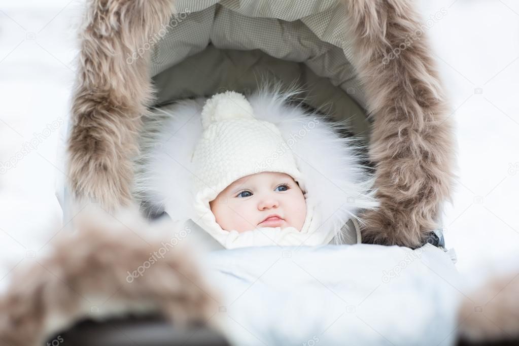 Sweet little baby sitting in a winter fur stroller