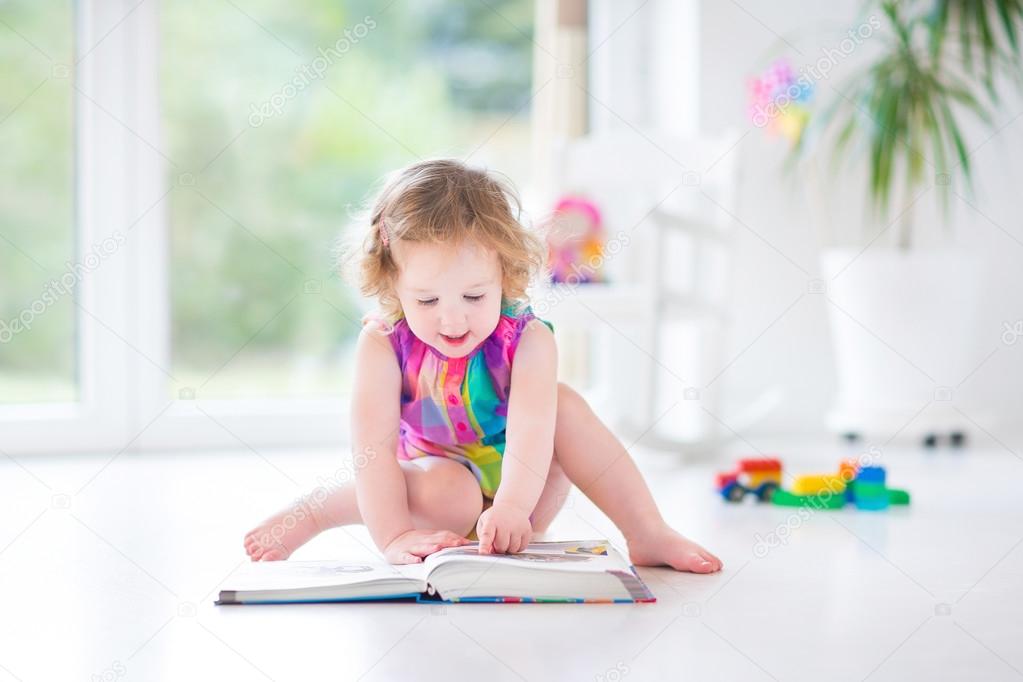 Toddler girl reading a book sitting on a fllor
