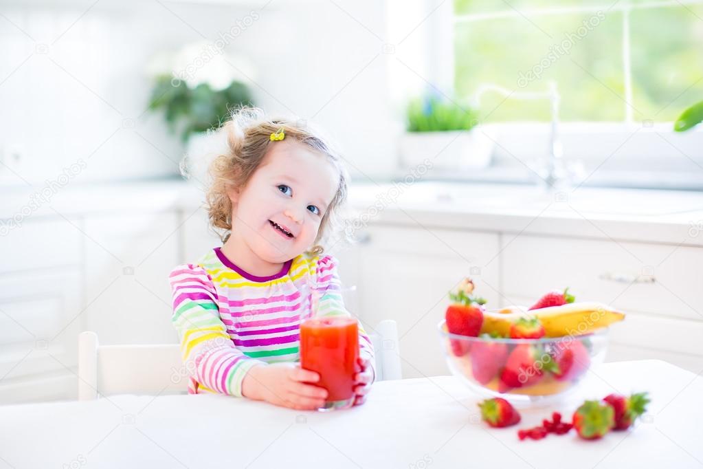 Toddler girl having breakfast drinking juice and eating corn flakes