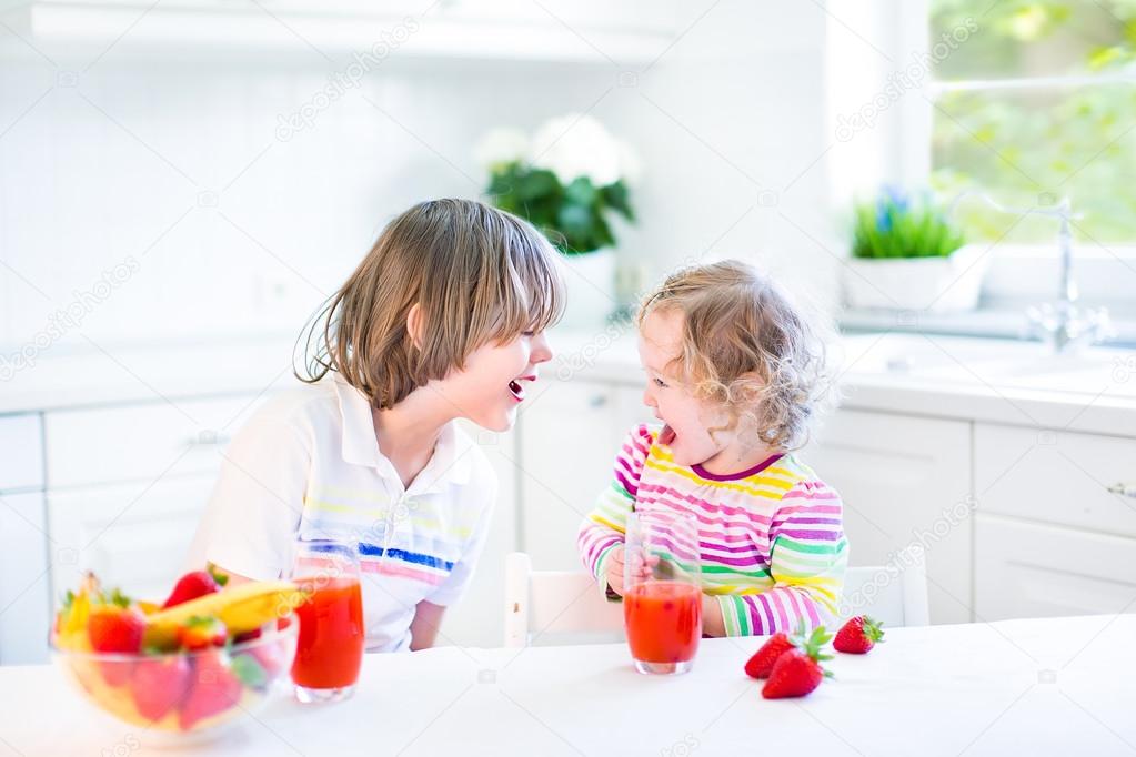 Happy teenager boy and his cute toddler sister having fruit for breakfast