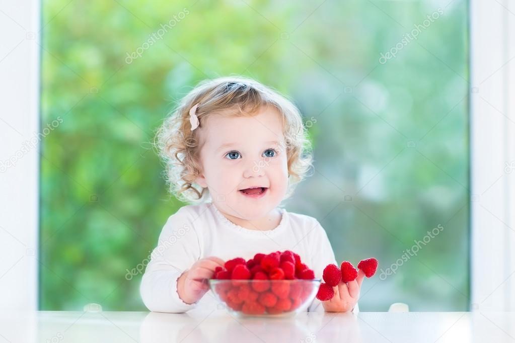 Cute toddler girl eating raspberries
