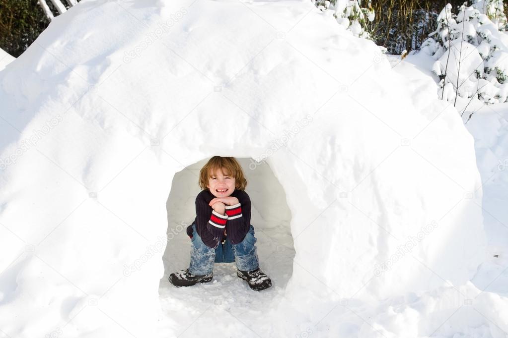 Boy playing in a snow igloo on a sunny winter day