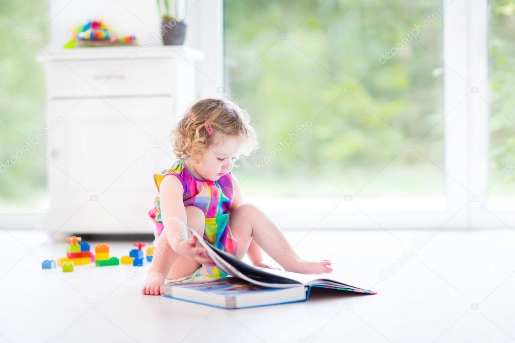 Toddler girl reading a book sitting on a floor