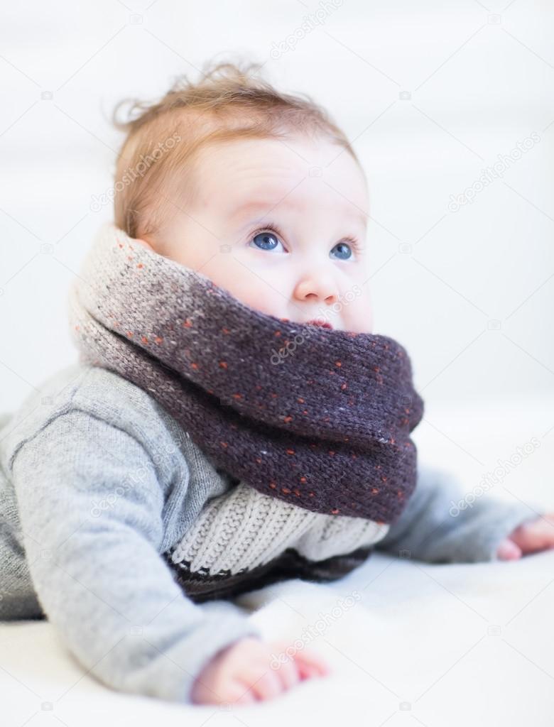 Baby in a frey knitted sweater and big brown scarf