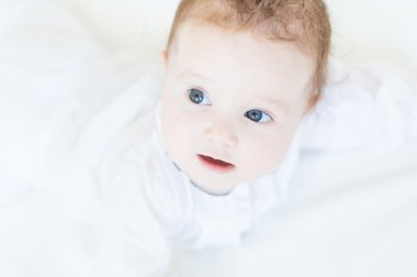 Beyaz elbiseli karnı üzerinde yatan bir kız bebek