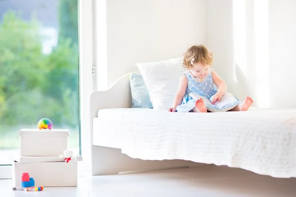 Маленькая девочка, сидящая на белой кровати — стоковое фото