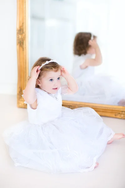 Toddler girl trying on a beautiful white dress next to a big mirror — Stock Photo, Image