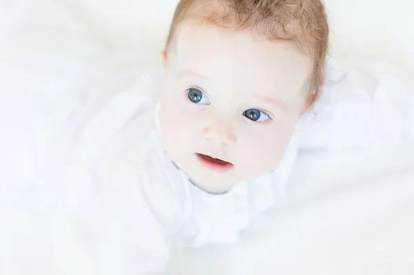 Bebê menina em um vestido branco deitado em sua barriga — Fotografia de Stock