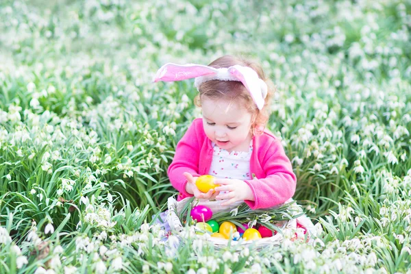女孩玩复活节彩蛋在白色的篮子里，坐在一个阳光明媚的花园 — 图库照片