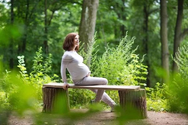 Atraktivní relaxační těhotná žena v parku — Stock fotografie