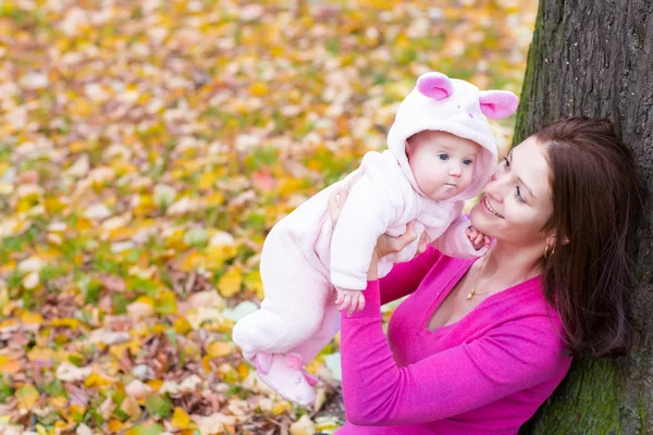 Mother holding her baby daughter under a tree — Stock Photo, Image