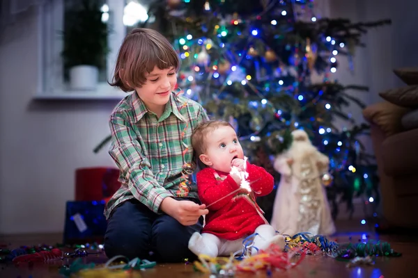Portrait of a brother and baby sister next to a Christmas tree — Stock Photo, Image