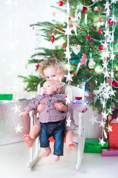 Peuter meisje en baby broer onder kerstboom — Stockfoto