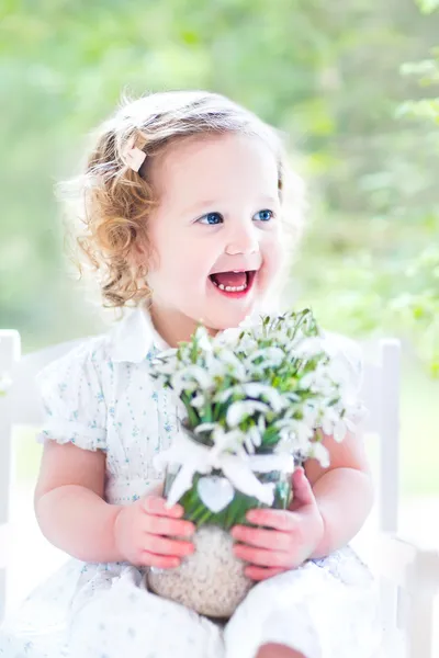 Girlsitting in a white rocking chair holding first spring flowers — Stock Photo, Image