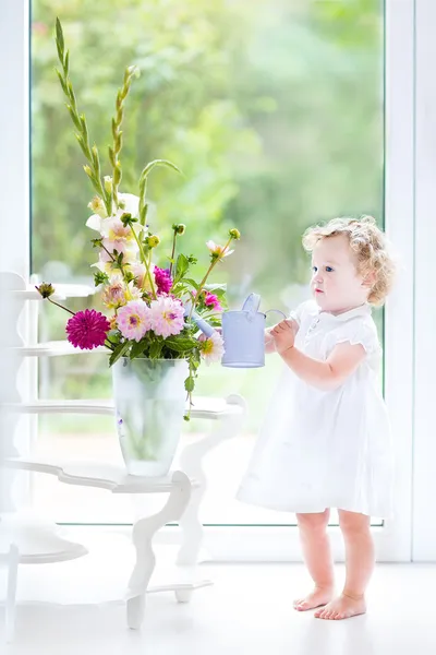 Toddler girl in a white dress watering flowers — Stock Photo, Image