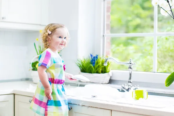 Chica lavando platos, limpiando con una esponja y jugando con espuma —  Fotos de Stock