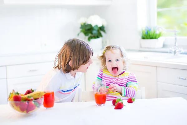 Glade tenåringsgutt og hans søte småbarnssøster som spiser frukt til frokost – stockfoto