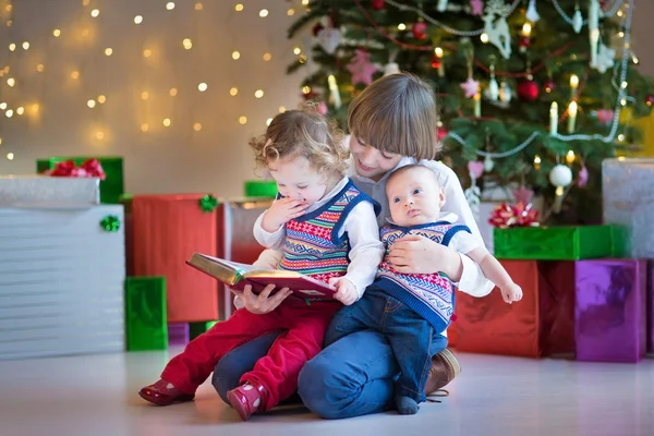 Garçon lisant à sa petite sœur et son petit frère nouveau-né — Photo