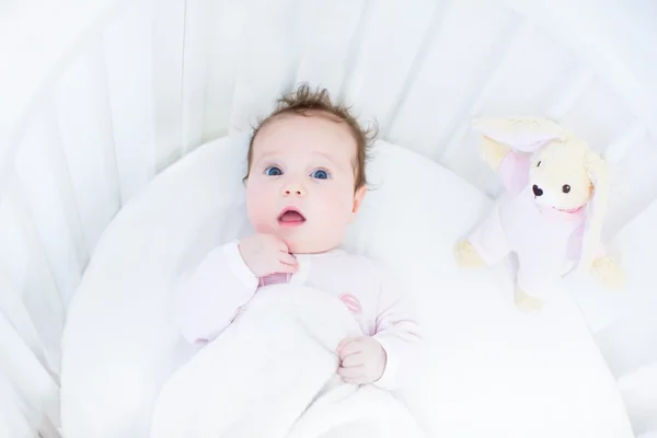 Bambina in una culla rotonda bianca con coniglietto rosa giocattolo — Foto Stock