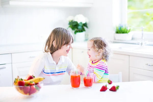 Nastolatek szczęśliwy chłopiec i jego siostra ładny maluch o owoce na śniadanie — Zdjęcie stockowe