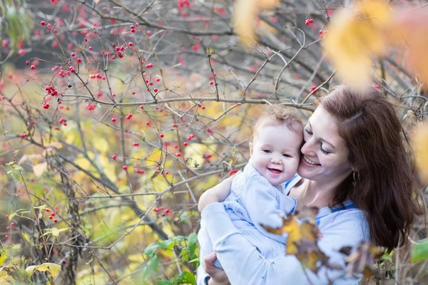 Mother hugging her baby under an ashberry bush — Stock Photo, Image