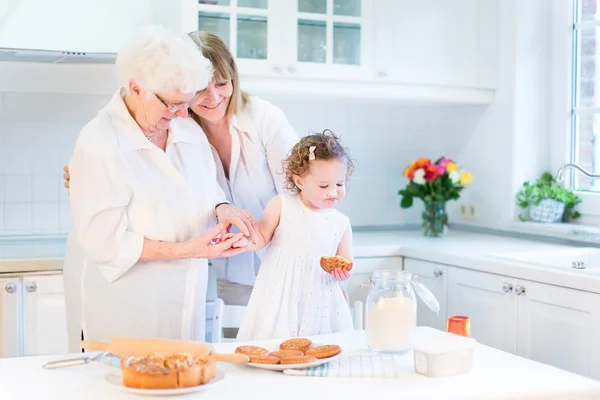 Woman baking a cake with her senior mother and cute toddler girl — Stock Photo, Image