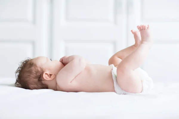 Pequeno bebê brincando com suas pernas e chupando em sua mão — Fotografia de Stock