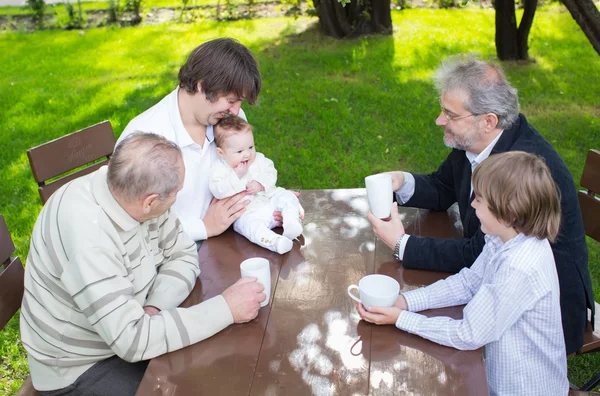 Four generations of one family sitting at a wooden table in the garden — Stock Photo, Image