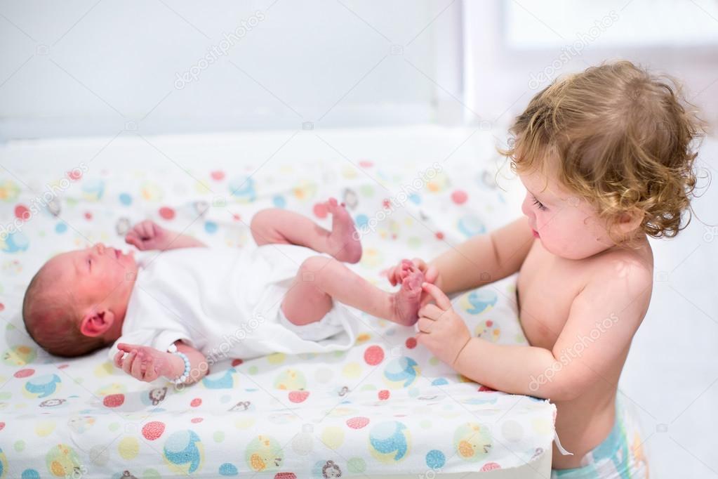 Toddler girl playing with the feet of her newborn baby brother